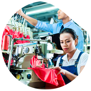 A woman sits concentrated at a sewing machine and works on a red fabric