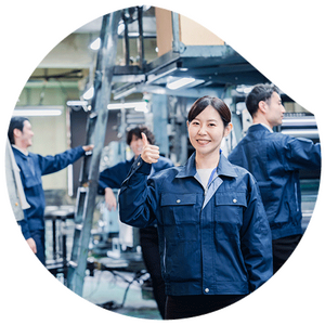 A woman in blue work clothes stands in a production hall and shows a thumbs up