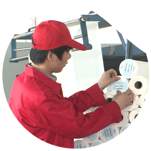 Worker in red uniform labeling yarn spools in a textile factory.