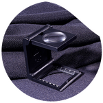 Thread counter magnifier on dark fabric for inspecting textile structure.