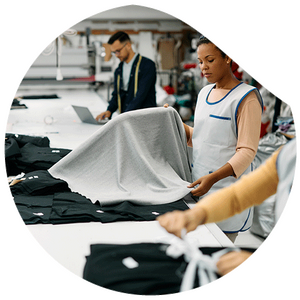 A woman stands at a work table and examines a grey fabric for its quality