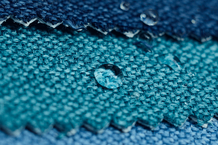 Close-up of several blue fabric swatches with zigzag edges and water droplets on a water-repellent surface.